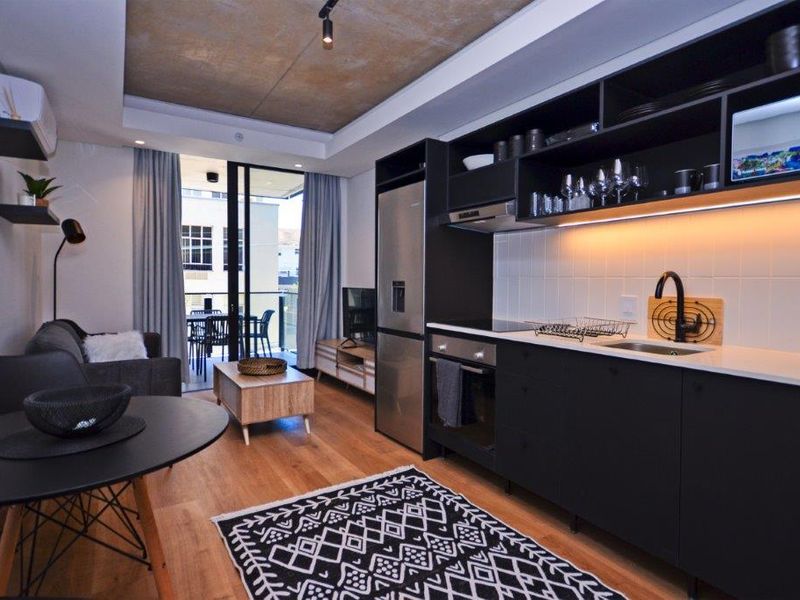 Modern open-plan apartment featuring a sleek kitchen with dark cabinetry, integrated appliances, and seamless flow to a private balcony.