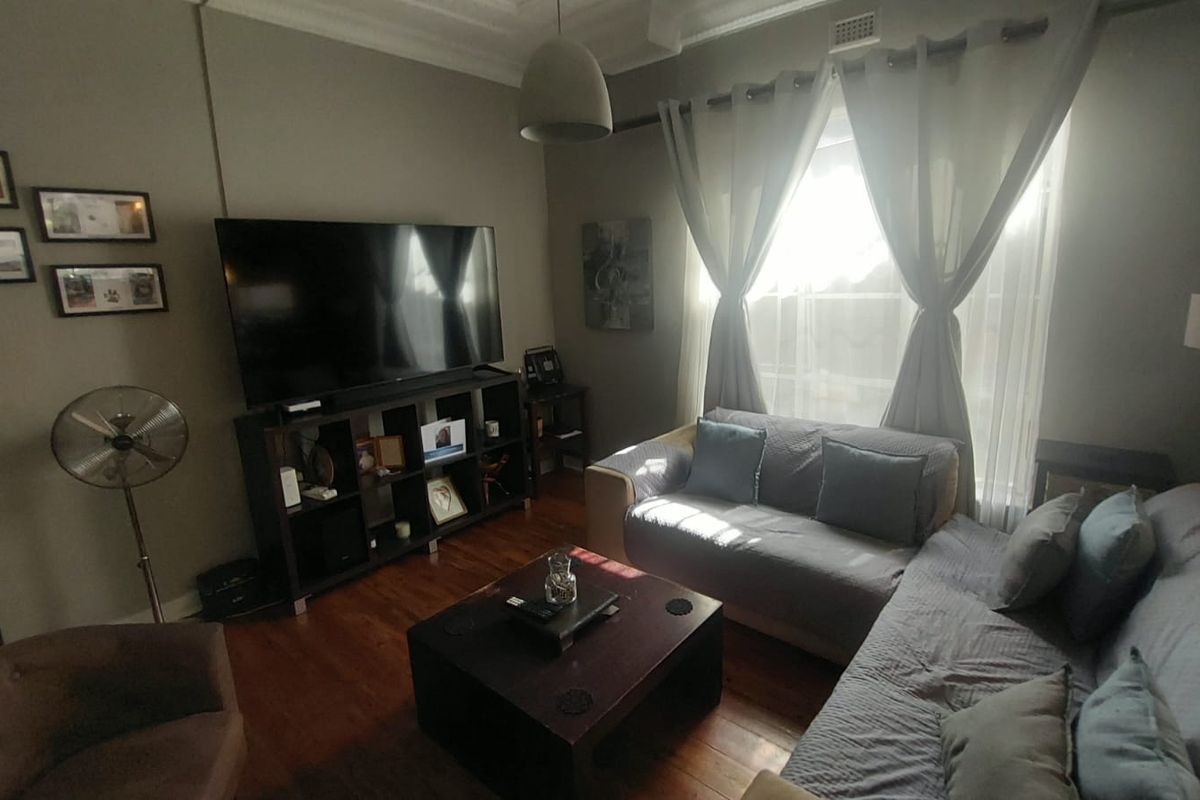 A comfortable living room featuring polished timber flooring, decorative ceiling cornices, and large windows that allow for ample natural light.