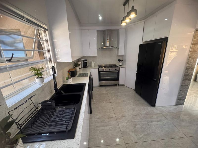 Modern kitchen featuring high-gloss white cabinetry, quartz countertops, a gas stove with stainless steel extractor, and sleek black fixtures on tiled flooring.