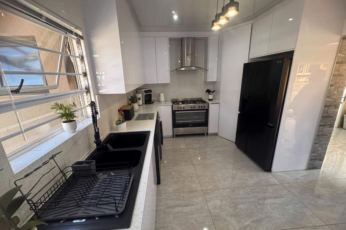 Modern kitchen featuring high-gloss white cabinetry, quartz countertops, a gas stove with stainless steel extractor, and sleek black fixtures on tiled flooring.