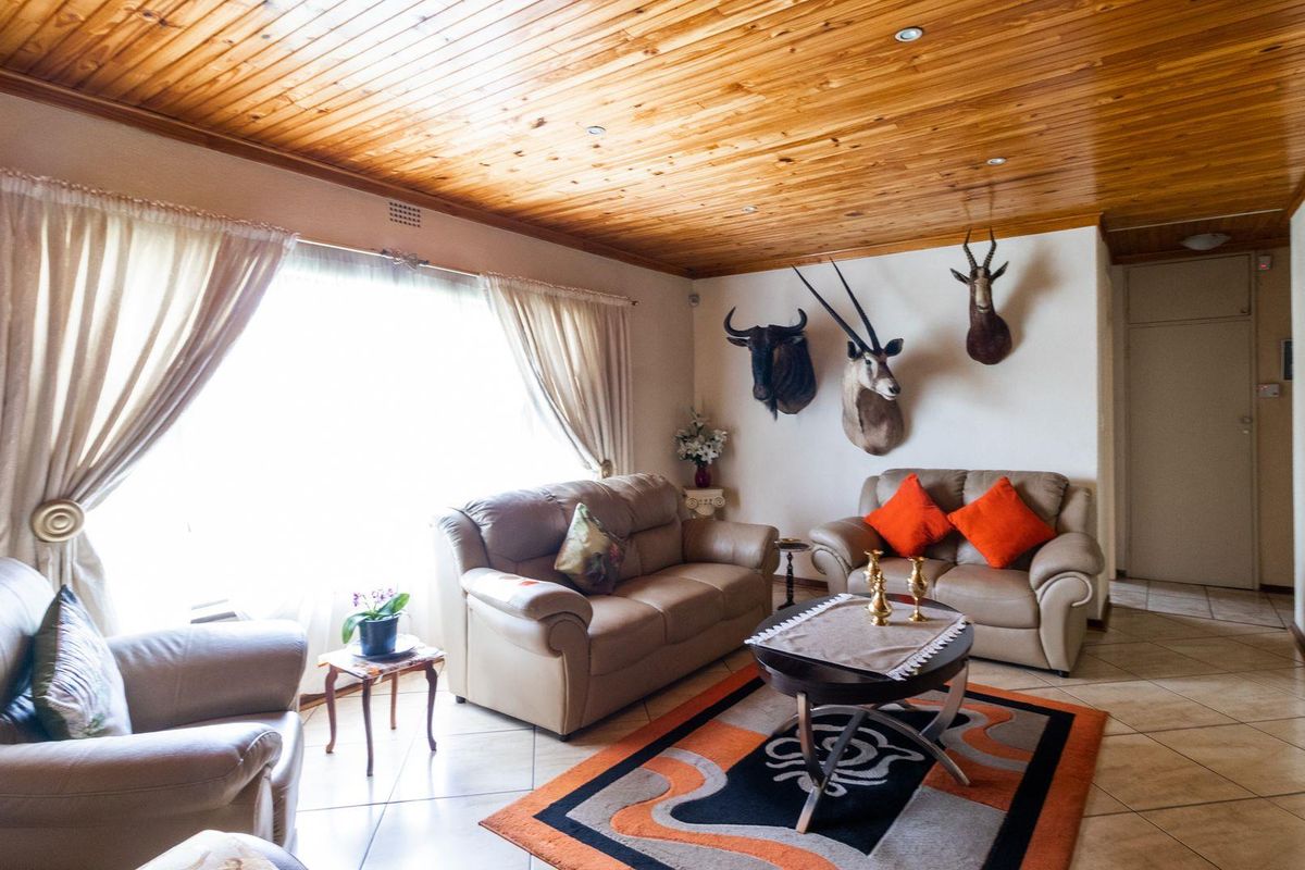 A living room featuring a distinctive timber-clad ceiling, tiled flooring, and large windows allowing for ample natural light.