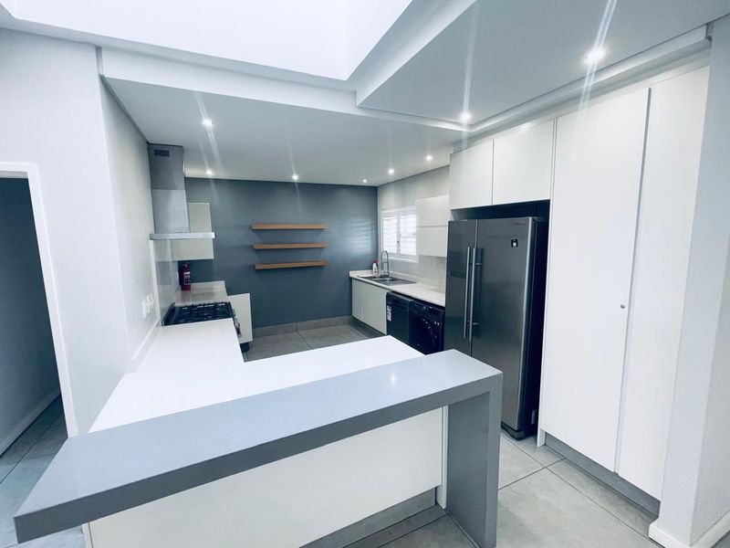 Modern kitchen featuring sleek white cabinetry, stone countertops, a gas hob with extractor, and a bright skylight, offering a clean and functional workspace.