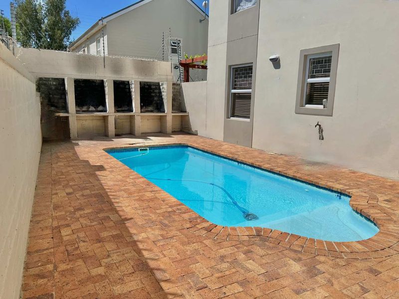Outdoor pool area featuring a rectangular swimming pool, brick paved surround, and a built-in triple braai station against the boundary wall.