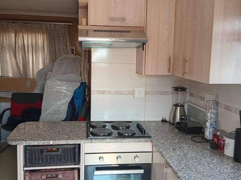A functional kitchen featuring light wood-finish cabinetry, granite countertops, a built-in oven, and an electric hob with an extractor fan.