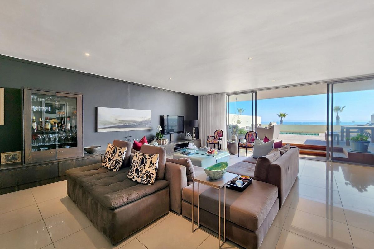 Spacious living room featuring large sliding glass doors that open onto a patio with ocean views, complemented by modern tiled flooring and recessed lighting.