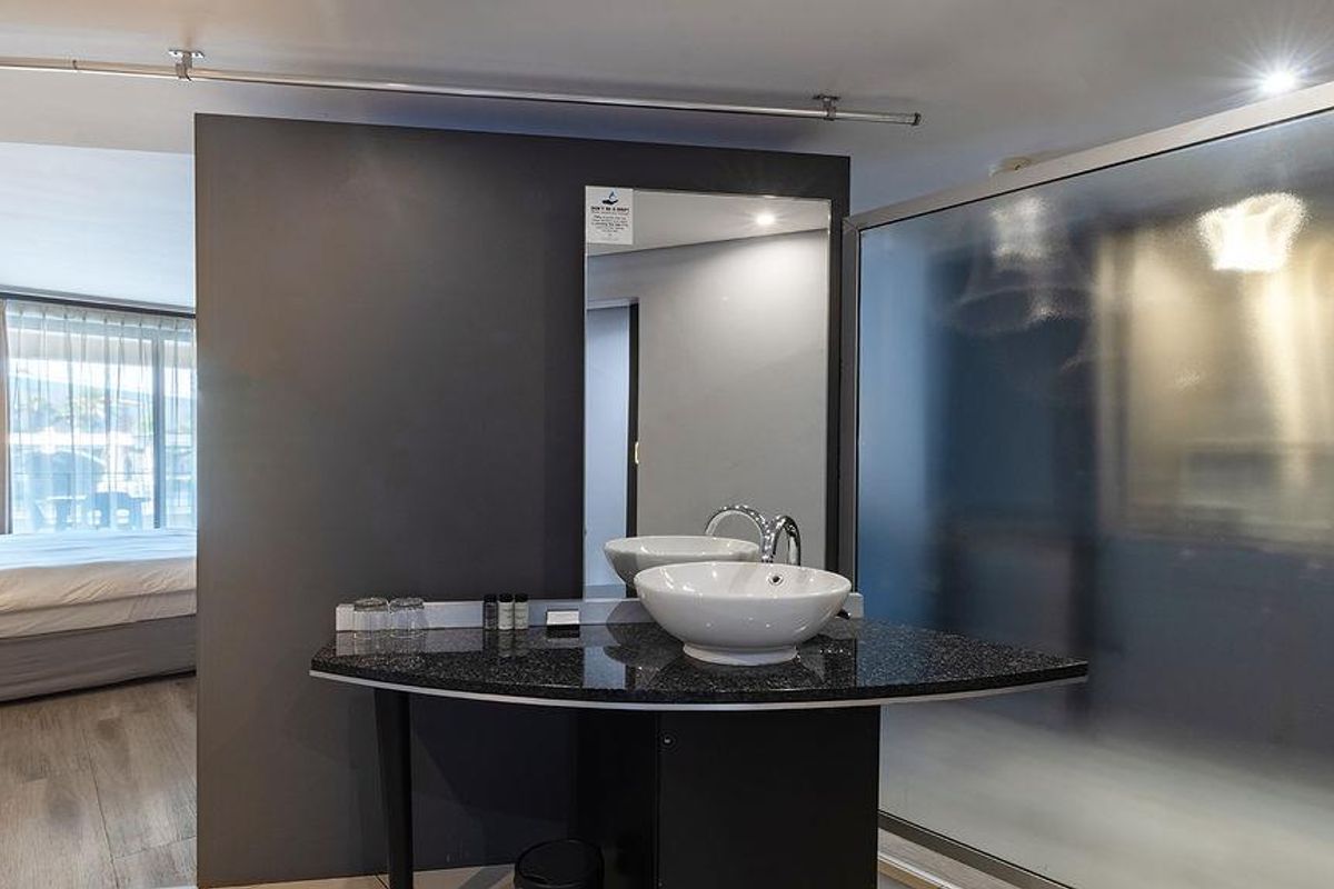 Modern open-plan bathroom area featuring a sleek granite vanity with a vessel sink and a frosted glass shower partition.