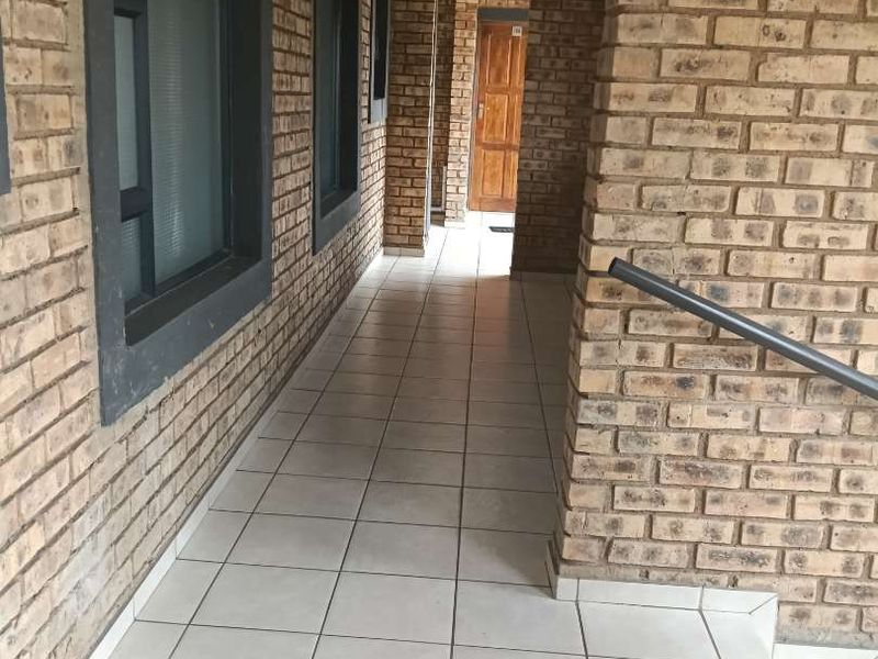 A clean, well-maintained exterior hallway featuring exposed brick walls, tiled flooring, and modern aluminium window frames.