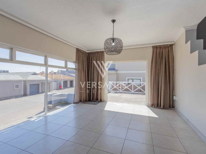Bright and spacious living area featuring large glass sliding doors leading to an outdoor patio, tiled flooring, and a staircase.