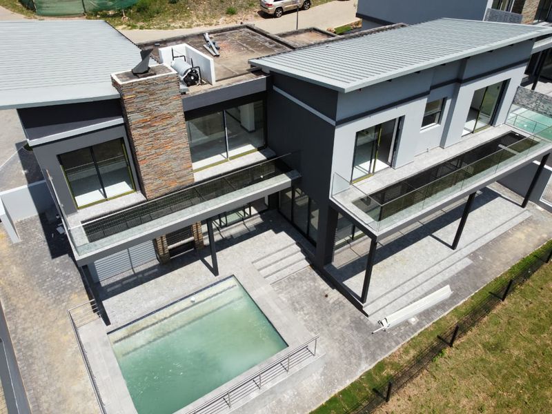 Aerial view of a modern cluster home featuring a swimming pool, paved patio area, stone-clad chimney, and upper-level balconies with glass balustrades.
