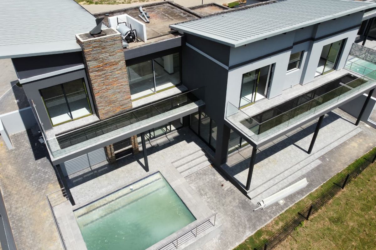 Aerial view of a modern cluster home featuring a swimming pool, paved patio area, stone-clad chimney, and upper-level balconies with glass balustrades.