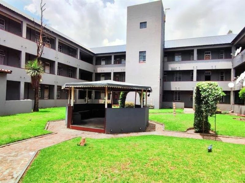 A view of the communal garden area and central gazebo within the apartment complex courtyard, featuring paved pathways and multi-story residential building wings.