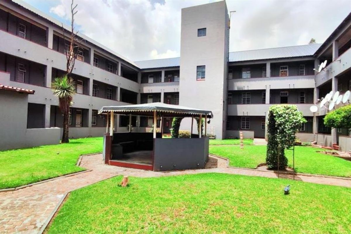 A view of the communal garden area and central gazebo within the apartment complex courtyard, featuring paved pathways and multi-story residential building wings.