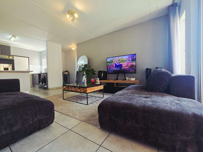 Open-plan living area featuring tiled flooring and a connected kitchen space with built-in cabinetry and appliances.
