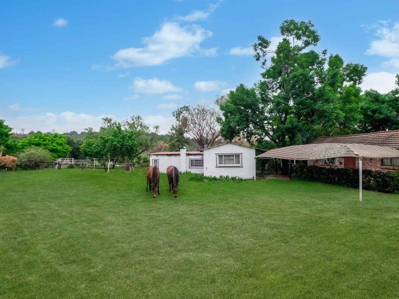 A spacious rear garden area featuring a large lawn, brick building structure, and a covered outdoor shade area on a farm property.