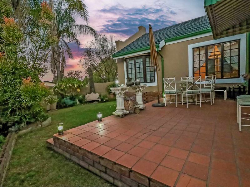 A covered patio area featuring terracotta tiling and a brick retaining wall, overlooking a landscaped garden with a sunset backdrop.