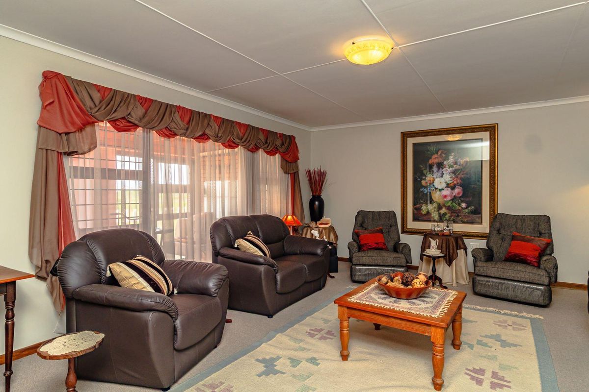 A spacious living room featuring large windows with drapes, neutral carpeting, and a central ceiling light fixture.
