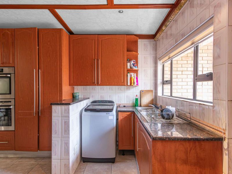 A functional scullery featuring wooden cabinetry, granite countertops, a stainless steel sink, and built-in oven and microwave units.
