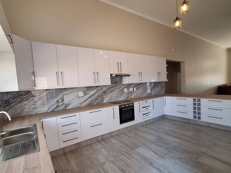 Modern kitchen featuring white gloss cabinetry, marble-look splashback, wood-look countertops, built-in oven, and tiled flooring in an open-plan layout.