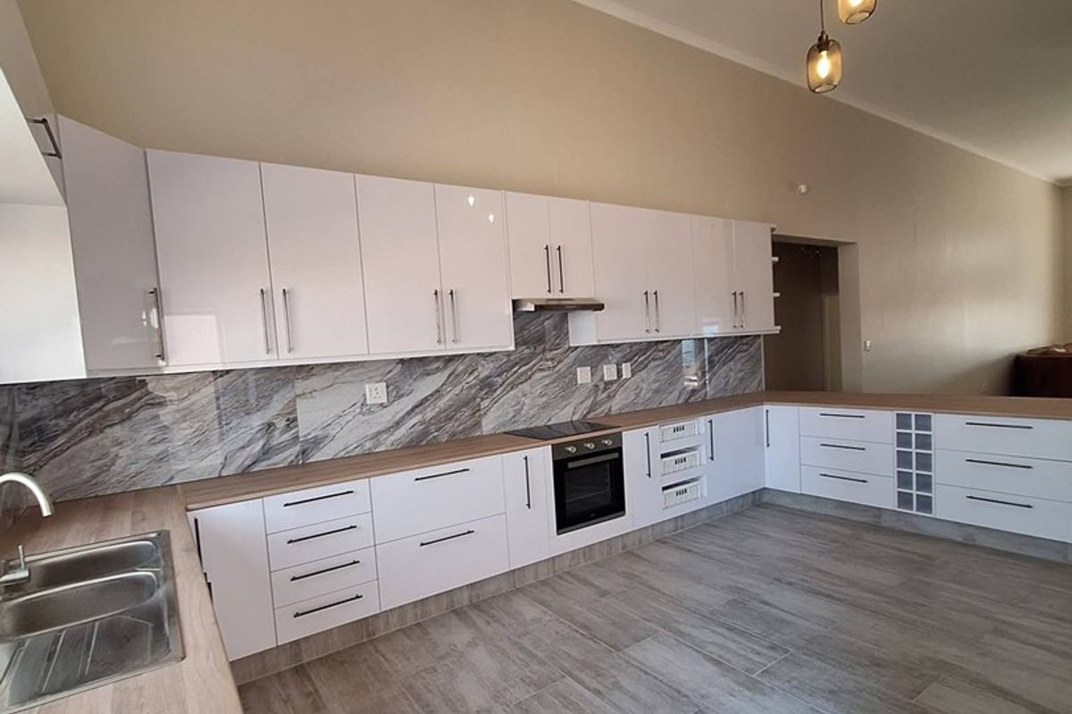 Modern kitchen featuring white gloss cabinetry, marble-look splashback, wood-look countertops, built-in oven, and tiled flooring in an open-plan layout.