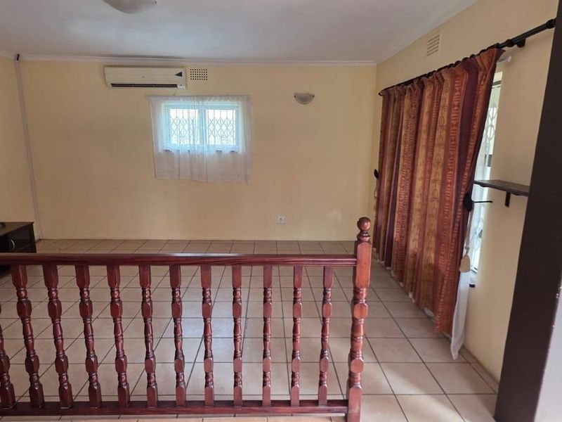 A living area featuring tiled flooring, a timber balustrade, and a wall-mounted air conditioning unit, with access to an outdoor space.