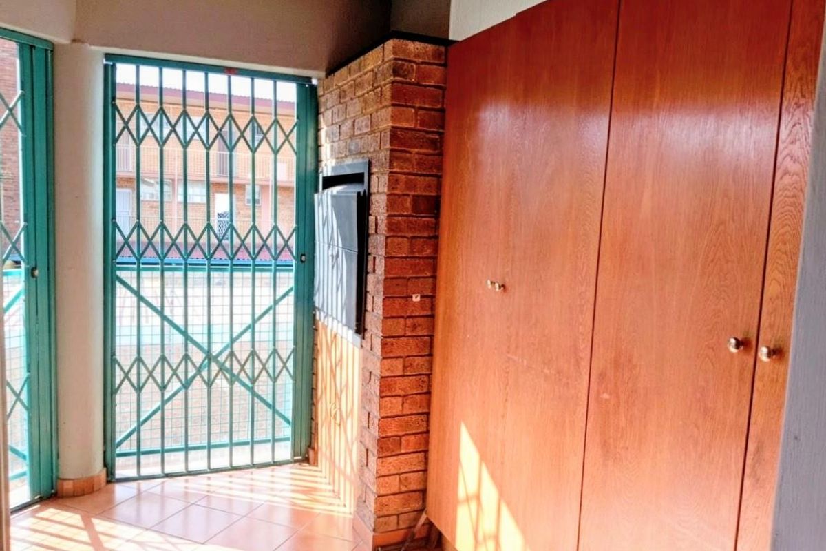 A covered patio area featuring built-in wooden storage cupboards, a brick pillar, tiled flooring, and a secure metal gate entrance.