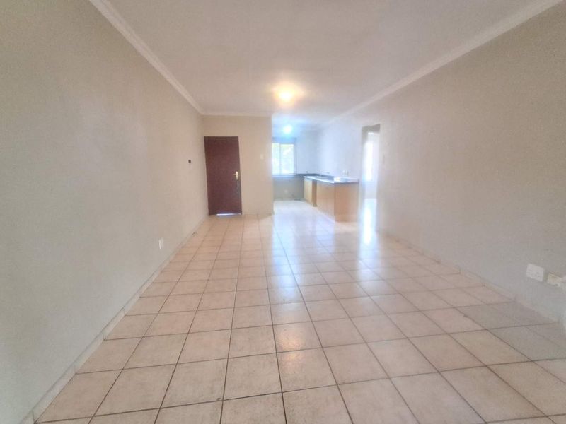An open-plan living and kitchen area featuring tiled flooring, neutral walls, and built-in kitchen cabinetry in a vacant apartment setting.