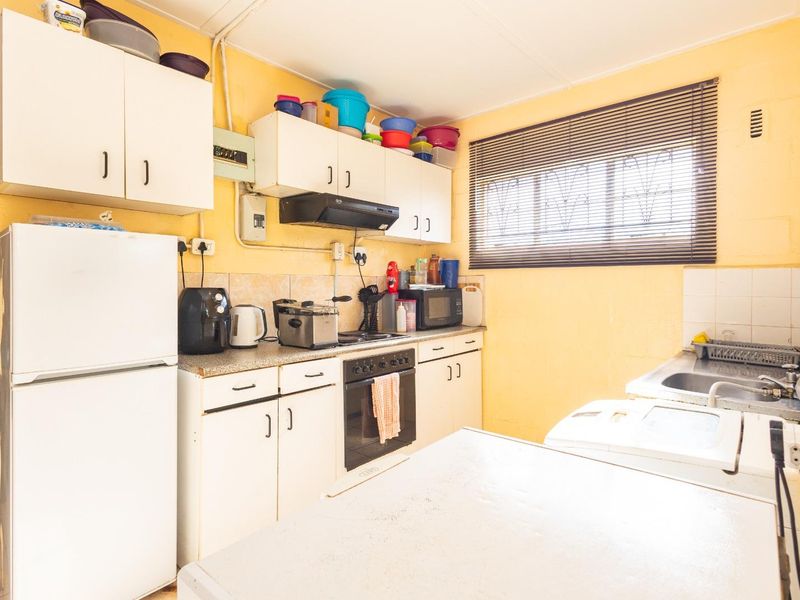 A functional kitchen featuring built-in cabinetry, an integrated oven and hob, extractor fan, and a stainless steel sink with tiled backsplash.