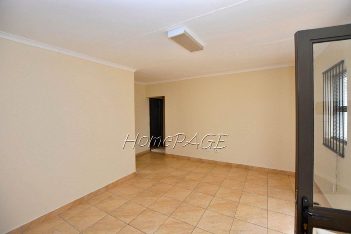 An empty living area featuring neutral wall paint, tiled flooring, and a secure door with integrated security bars.