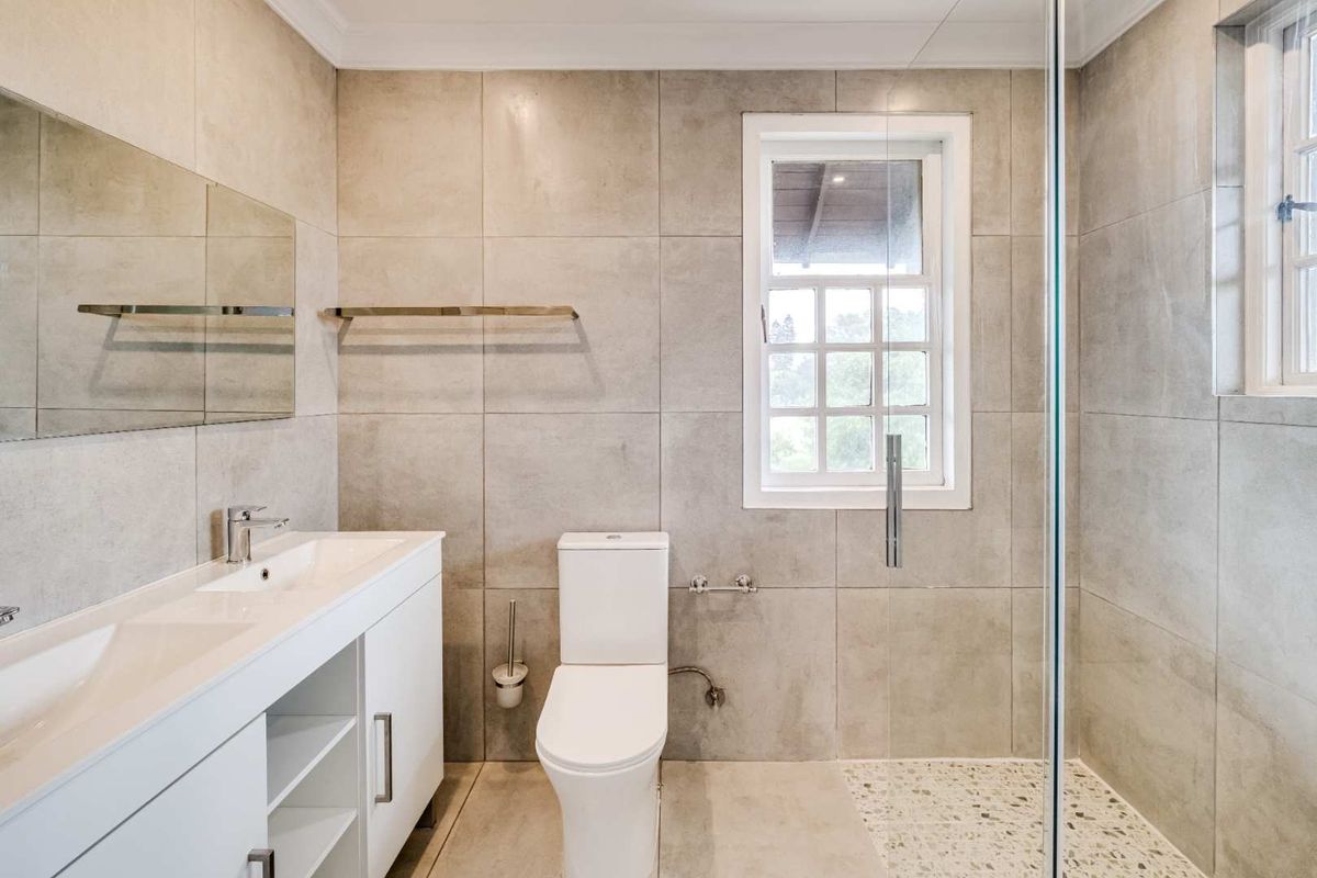 Modern bathroom featuring a sleek white vanity, integrated basin, glass-enclosed shower, and neutral large-format wall tiles with a clean, contemporary finish.