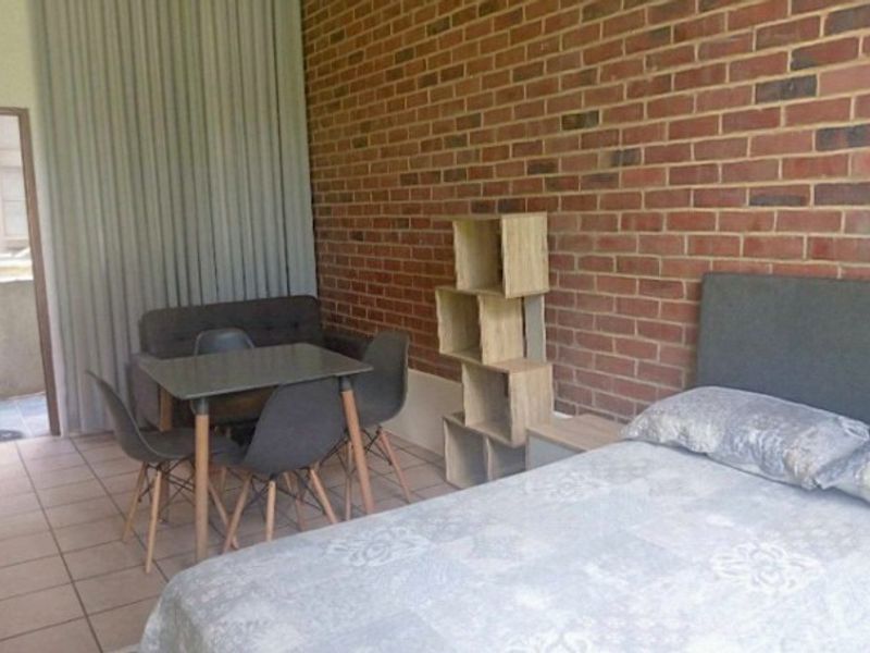 A bedroom featuring an exposed brick feature wall, tiled flooring, and access to an outdoor area through a sliding door.
