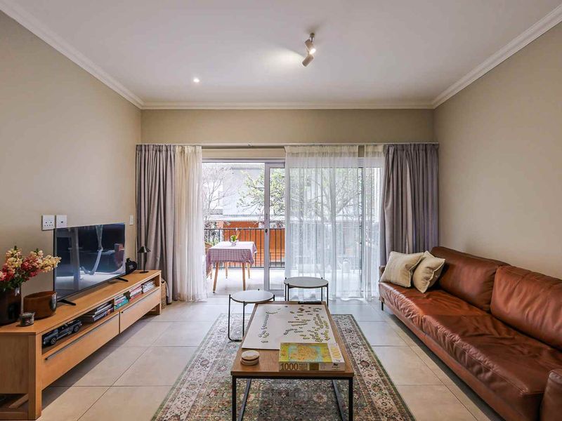 A well-maintained living room featuring neutral tiled flooring, cove cornicing, and a large sliding glass door providing access to an outdoor balcony area.