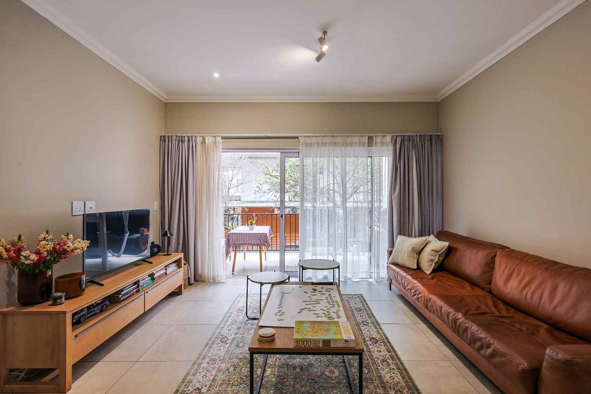 A well-maintained living room featuring neutral tiled flooring, cove cornicing, and a large sliding glass door providing access to an outdoor balcony area.