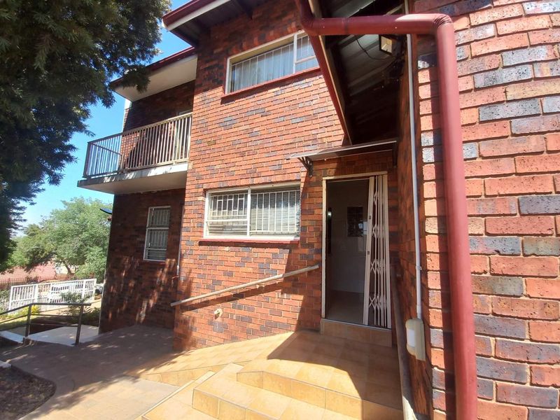 Front entrance of a face brick house featuring tiled steps, a metal security gate, and an upper-level balcony with metal railings.