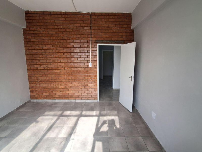 An empty bedroom featuring an exposed brick accent wall, neutral grey painted walls, and ceramic floor tiling.