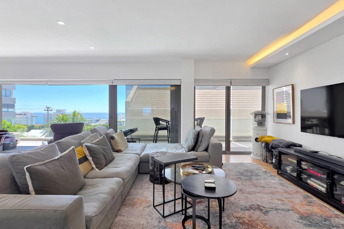 Spacious living room featuring recessed and cove lighting, hardwood floors, and large sliding glass doors that open to a balcony with coastal views.