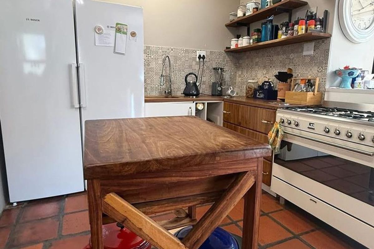 A functional kitchen featuring wooden cabinetry, a gas stove, open shelving, and terracotta floor tiles, providing a rustic and practical cooking space.