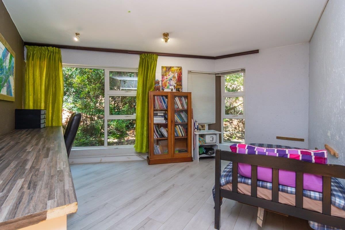A bedroom featuring light-toned laminate flooring, large windows with garden views, and a built-in desk area.