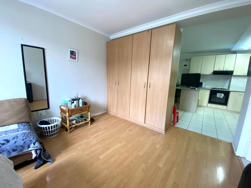 Open plan living area featuring laminate flooring, a large built-in wardrobe, and an adjacent kitchen with fitted cabinetry and built-in appliances.