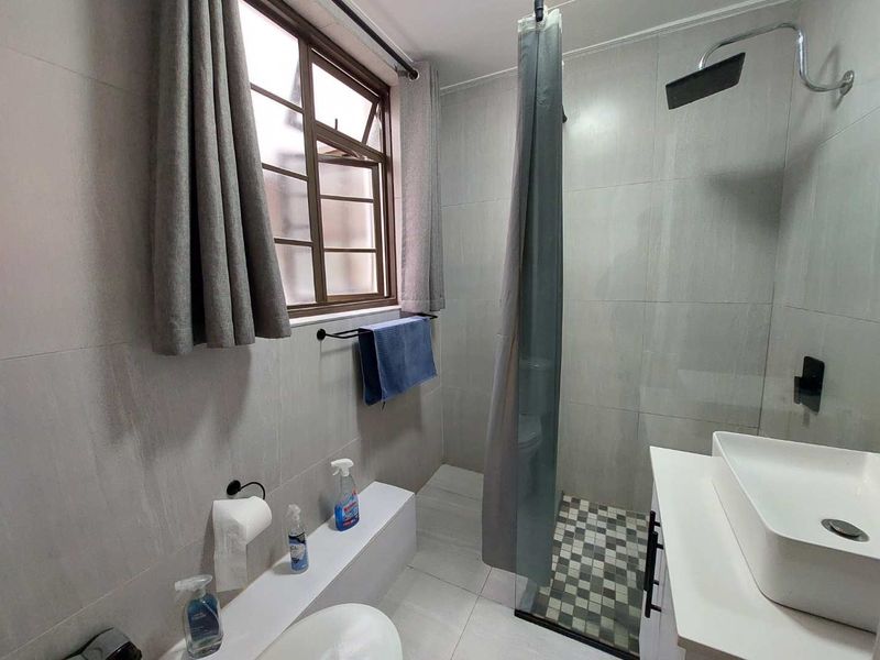 A modern bathroom featuring tiled walls, a vessel sink, and a shower area with a mosaic floor detail.