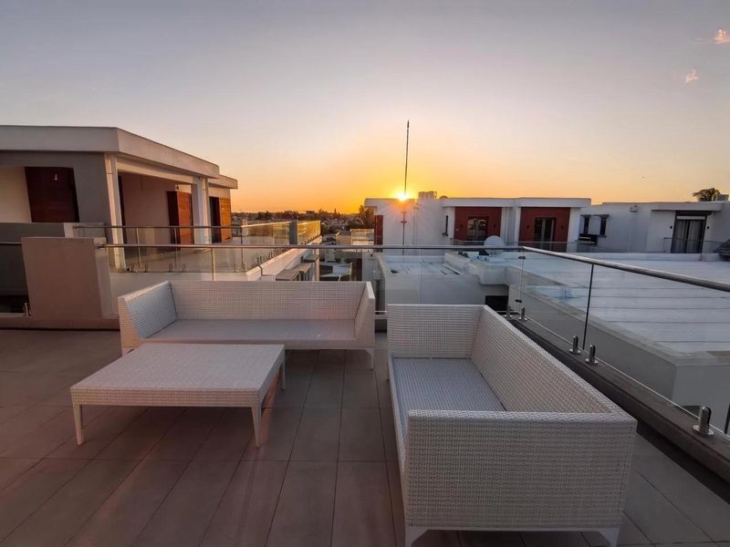 Spacious rooftop balcony featuring modern glass balustrades and tiled flooring, offering an elevated outdoor living space with sunset views.