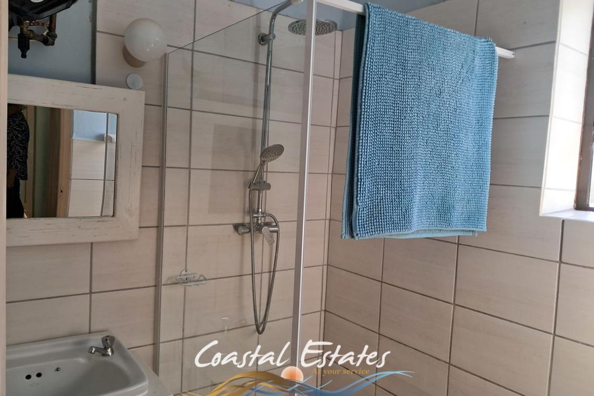 A bathroom featuring a glass-enclosed shower with a rainfall showerhead, a wall-mounted basin, and tiled walls.