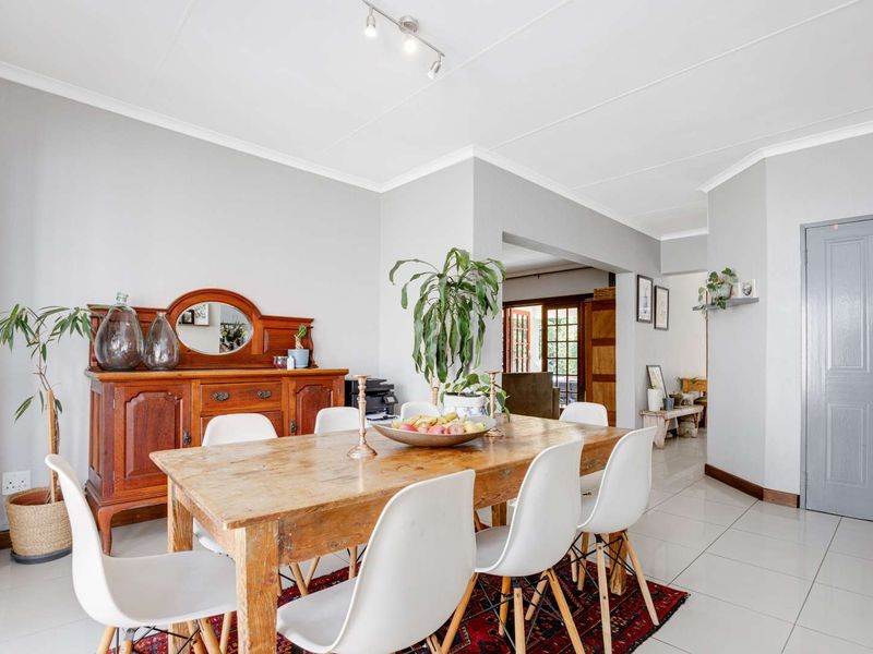 A bright and well-maintained dining room featuring neutral wall tones, tiled flooring, and modern track lighting, with an open flow to adjacent living spaces.