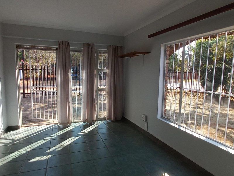 A bright, empty living room featuring tiled flooring, large windows with security bars, and a sliding glass door leading to the exterior.