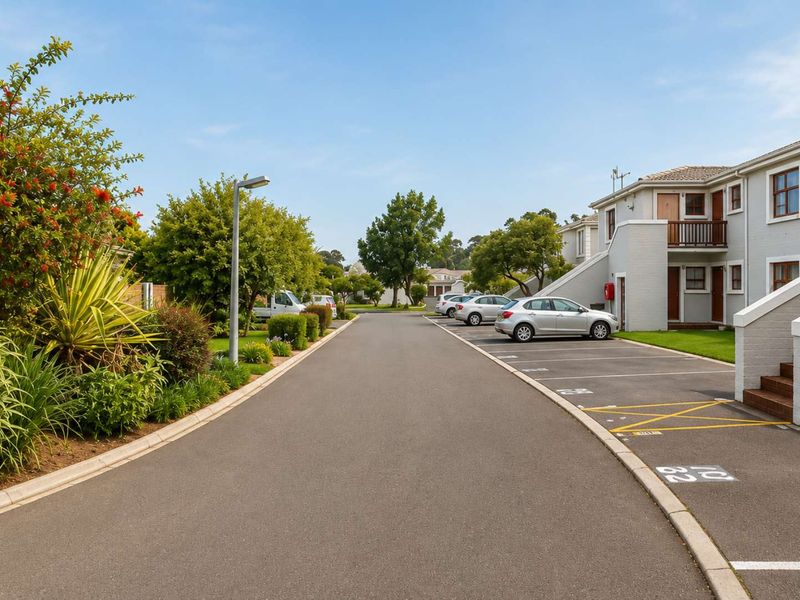 A well-maintained apartment complex exterior featuring paved parking bays, landscaped garden areas, and clear access to the residential building units.
