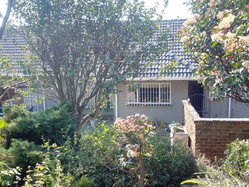 A view of the rear exterior of the house featuring a tiled roof, security bars on windows, and a stone pathway leading through the garden.