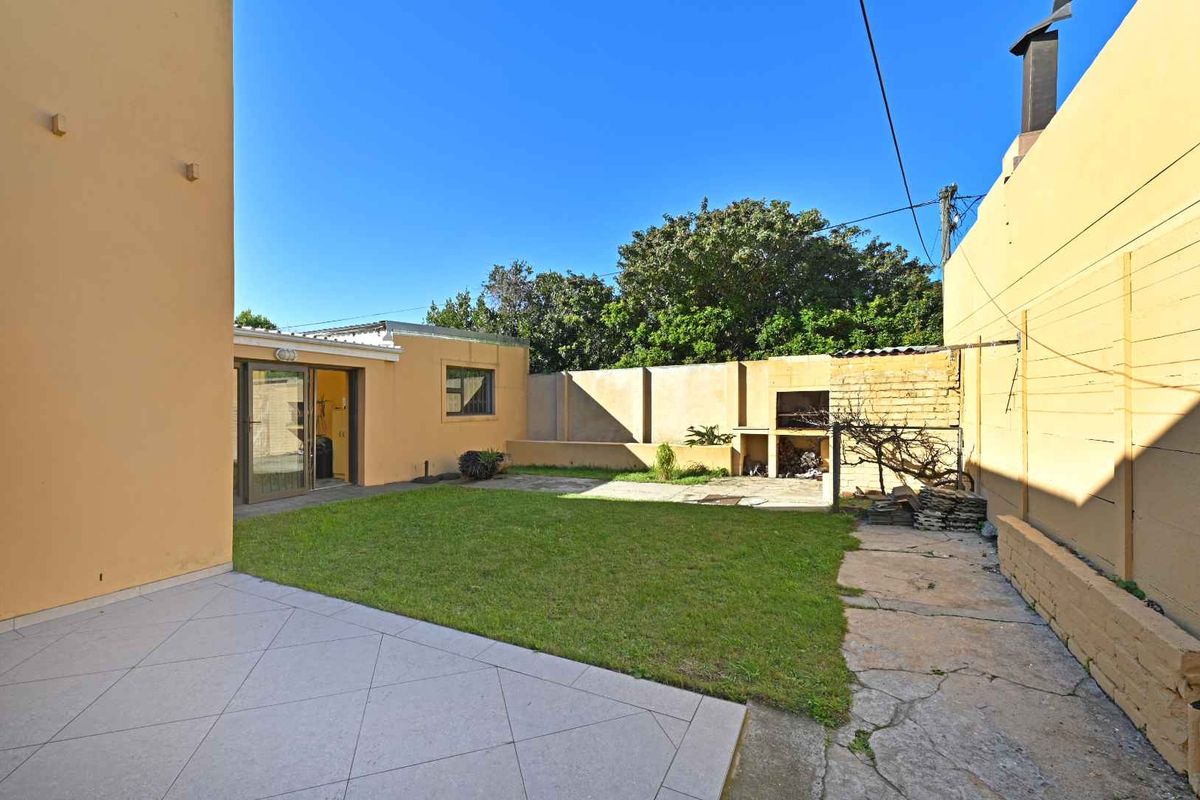 Rear garden area featuring a paved patio, lawn, and a built-in outdoor braai facility against the boundary wall.