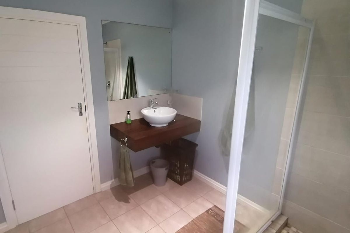 A modern bathroom featuring a floating wooden vanity with a vessel sink, a large wall-mounted mirror, and a glass-enclosed shower with tiled flooring.
