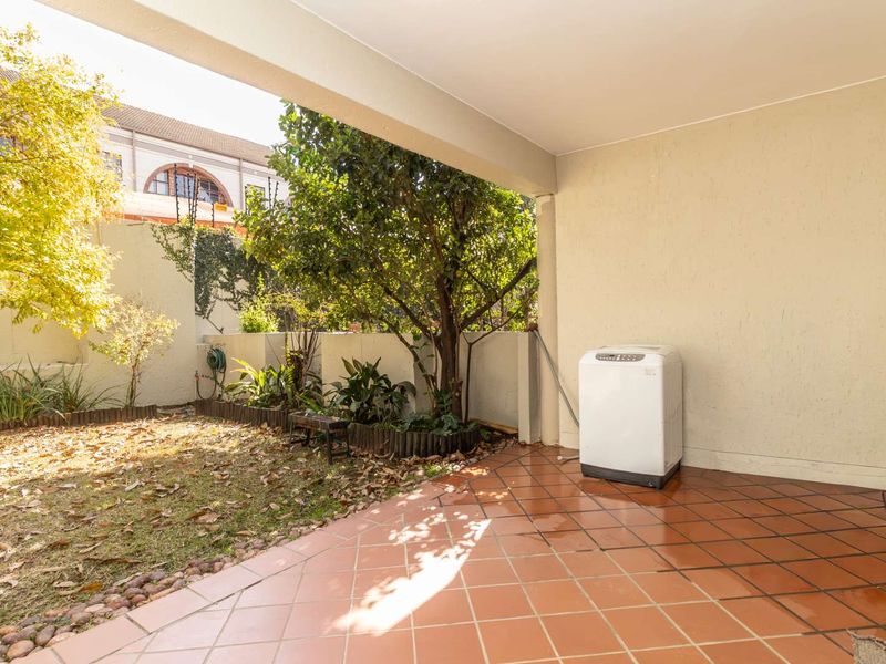 A covered patio area with tiled flooring, overlooking a private garden space with boundary walls.