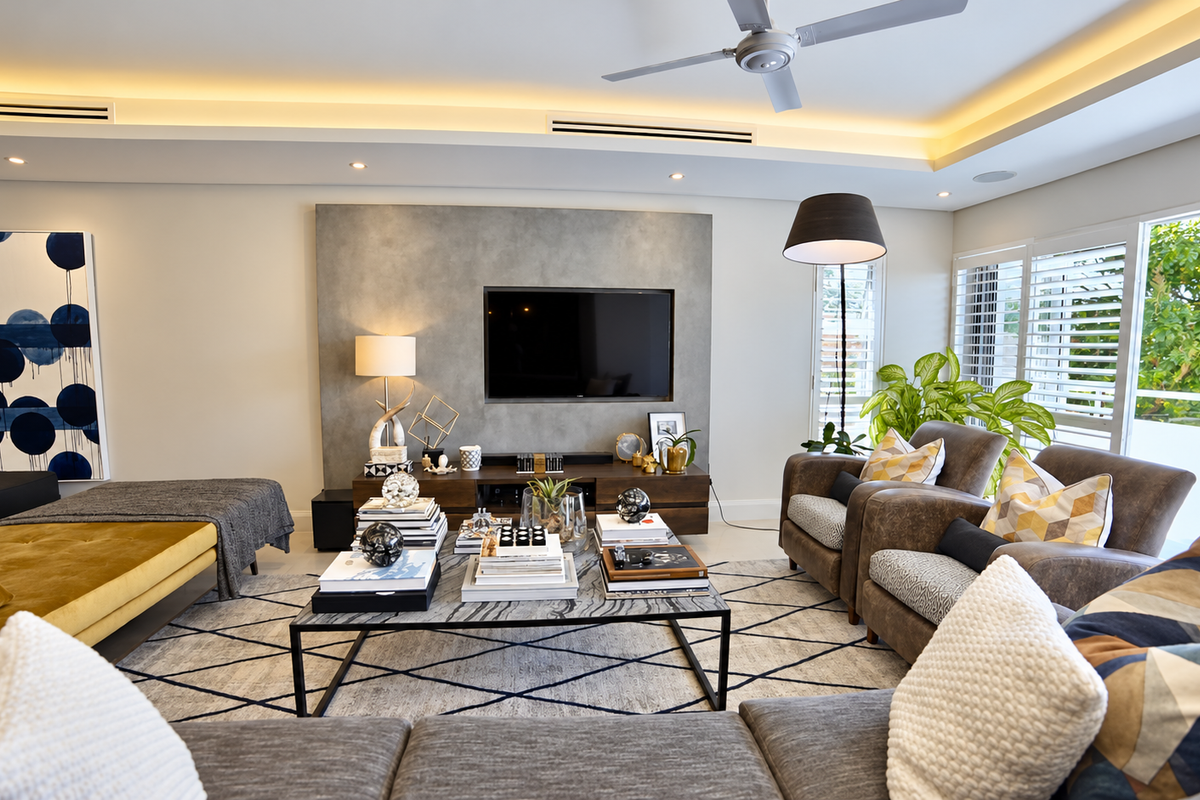 A modern, well-appointed living room featuring a feature wall, recessed ceiling lighting, ducted air conditioning, and plantation shutters opening to an outdoor area.