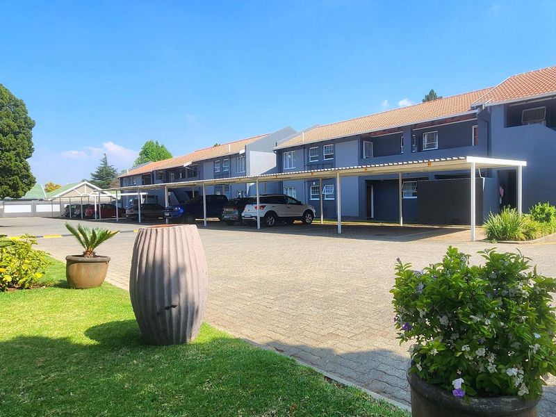 Exterior view of a townhouse complex featuring a paved driveway, covered parking bays, and well-maintained garden areas.